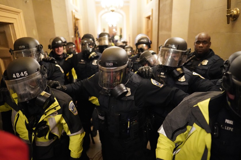 一群穿着军装的人：1月6日的暴动期间，身穿防暴服的警察清理了国会大厦内的走廊。（肯特·西村/洛杉矶时报）
