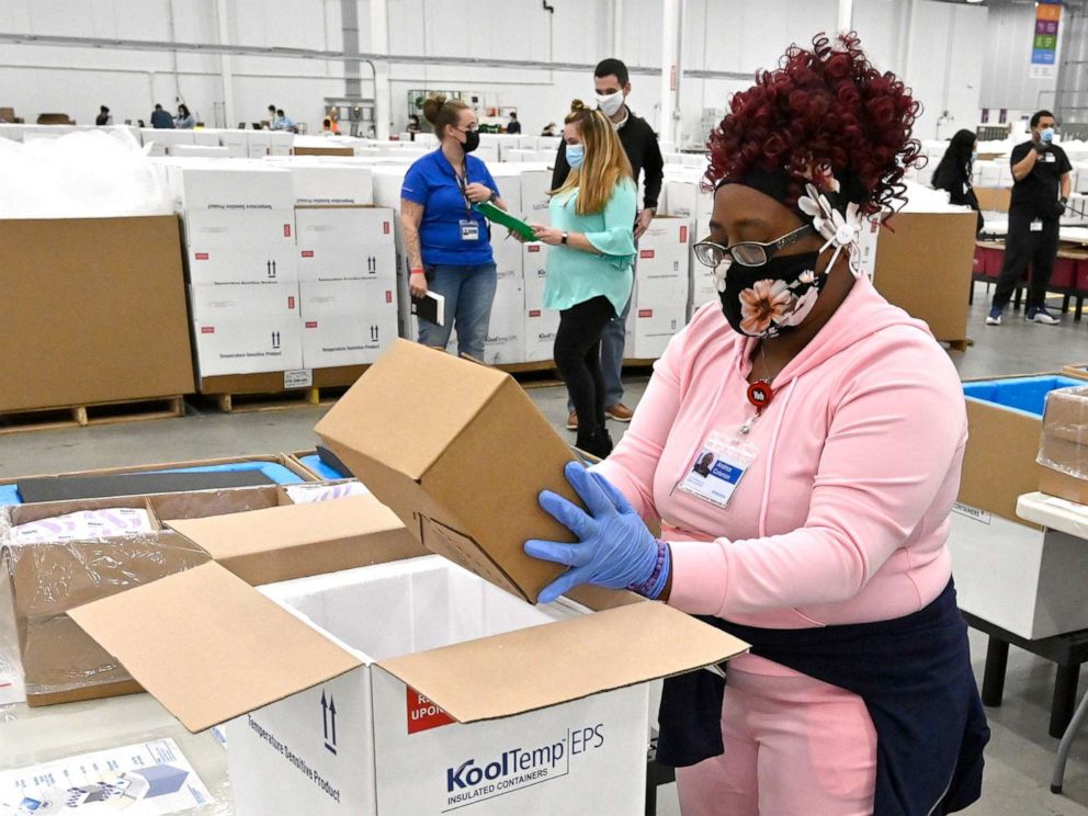 一群人坐在箱子里：麦基森公司的一名员工将一盒强生公司的Johnson and Johnson COVID-19疫苗装进一个冷藏箱中，以便于2021年3月1日从他们在肯塔基州谢泼兹维尔的工厂装运。