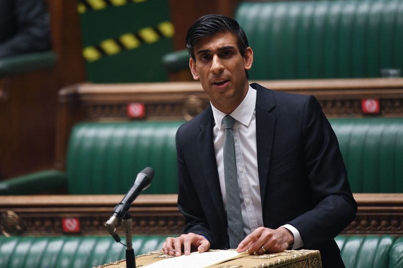 一个穿着西服打着领带的男人坐在椅子上：财政大臣Rishi Sunak向伦敦下议院交付预算。